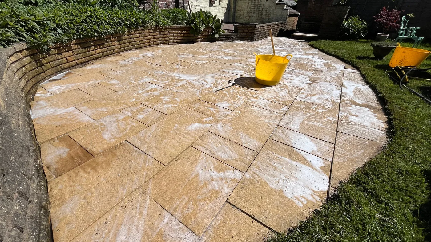 Curved sandstone patio during a professional chemical cleaning treatment showing soap foam being brushed on the surface